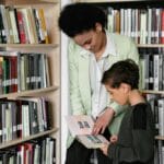 Dorosły pomaga dziecku czytać książkę w bibliotece