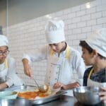 Dzieci w kuchni rozsmarowują sos pomidorowy na pizzy podczas zabawy
