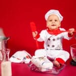 Niemowlę w czapce kucharskiej bawi się akcesoriami kuchennymi