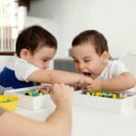 Dwóch chłopców bawi się drewnianymi koralikami w domu