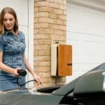 Kobieta podłącza ładowarkę do samochodu elektrycznego przy domu