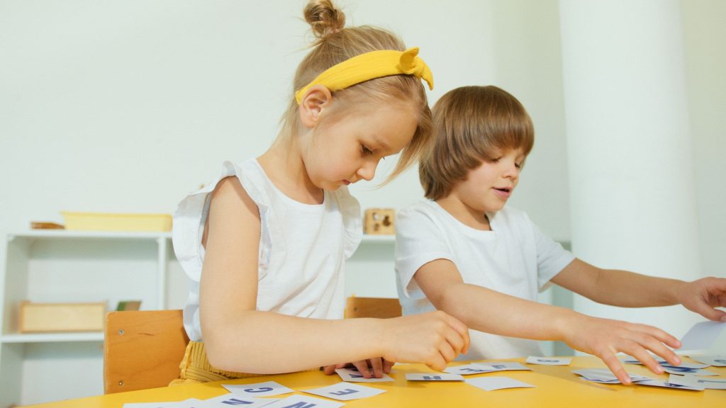 Dwoje dzieci podczas zabawy edukacyjnej z literami w sali przedszkolnej