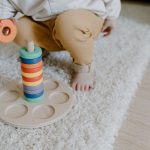 Dziecko układa drewniane krążki na dywanie w sali przedszkolnej